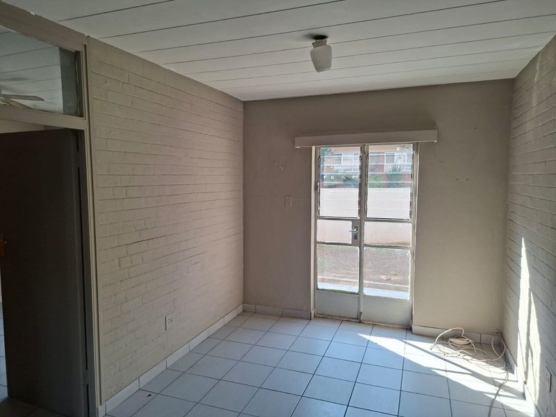 An empty living area featuring tiled flooring, exposed brick walls, and a glass panel door providing natural light and exterior access.