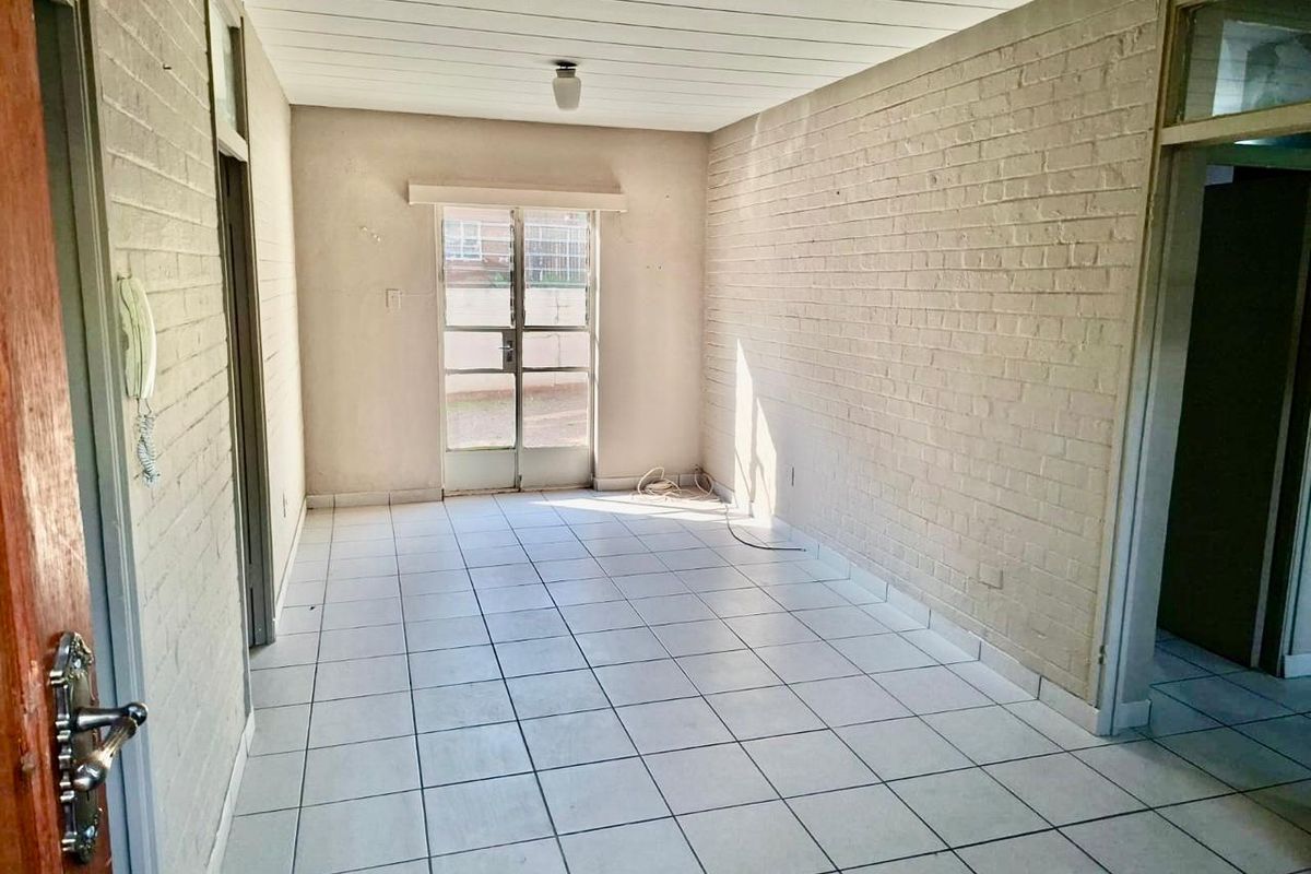 An empty living room featuring white painted brick walls, tiled flooring, and a sliding door leading to the exterior.