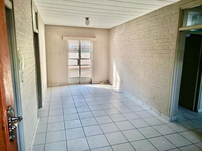 An empty living room featuring white painted brick walls, tiled flooring, and a sliding door leading to the exterior.