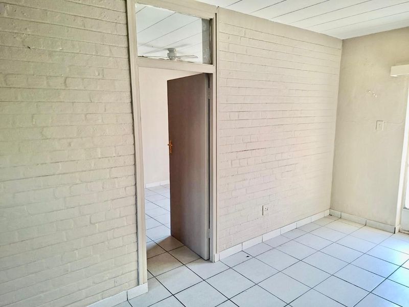 An empty living area featuring painted brick walls, tiled flooring, and a ceiling fan, providing a blank canvas for interior design.