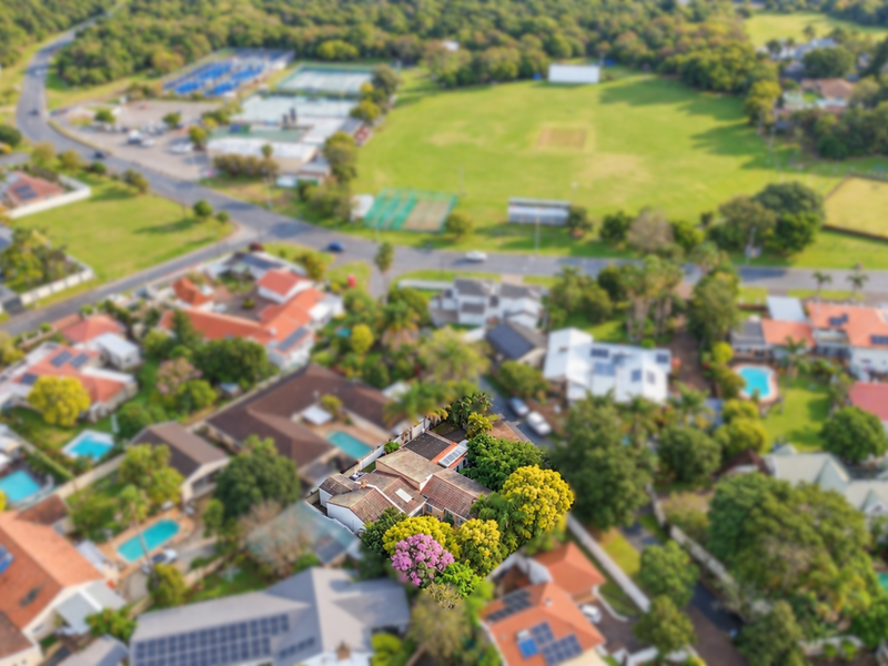 An aerial view of the property highlighting its roof structure, solar panel installation, and surrounding landscaped garden within the residential neighborhood.