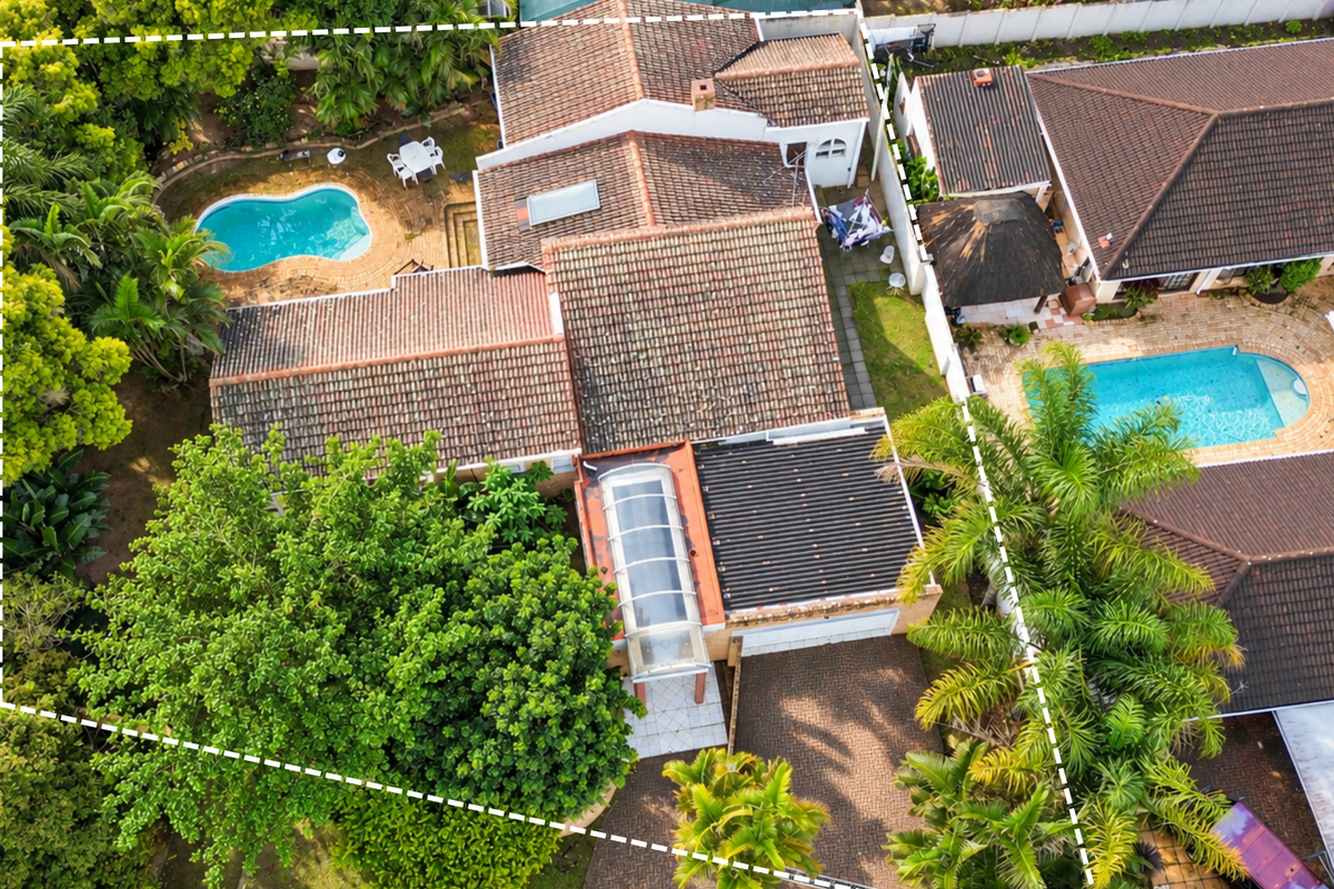 Aerial view of the property featuring a tiled roof, swimming pool, paved driveway, and established garden landscaping within the boundary.