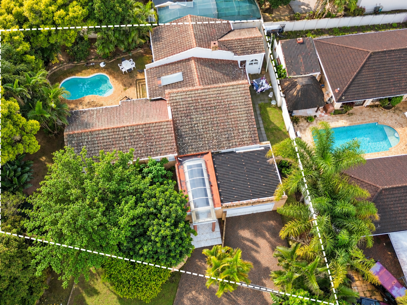 Aerial view of the property featuring a tiled roof, swimming pool, paved driveway, and established garden landscaping within the boundary.