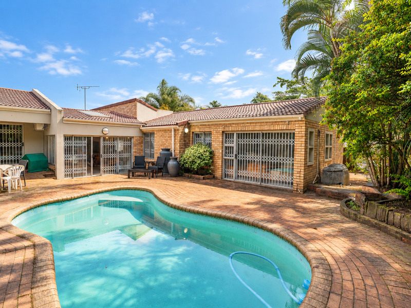 Outdoor pool area featuring brick paving, established garden surroundings, and direct access to the home through sliding glass doors with security gates.