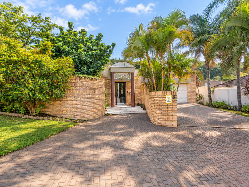 Front view of a residential property featuring a brick facade, paved driveway, and a covered entrance with established landscaping.