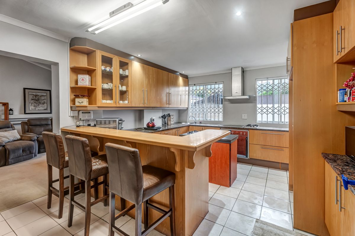 Functional kitchen featuring wooden cabinetry, a breakfast bar, built-in oven, hob, and stainless steel extractor fan, with tiled flooring throughout.