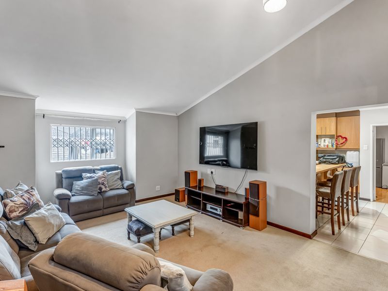Open-plan living area featuring a vaulted ceiling, carpeted lounge space, and an adjacent kitchen with tiled flooring and built-in cabinetry.