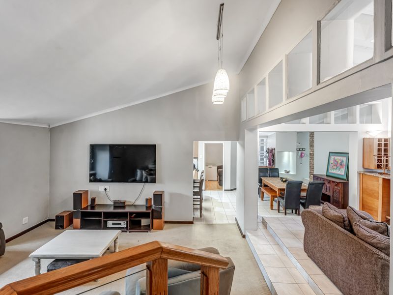 Spacious open-plan living and dining area featuring vaulted ceilings, clerestory windows, and a split-level layout with a mix of carpet and tile flooring.