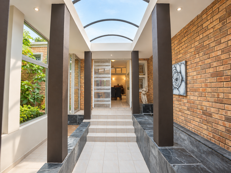 A bright and modern entrance hall featuring a unique arched glass roof, exposed brick walls, and elegant tiled flooring leading to the main living area.