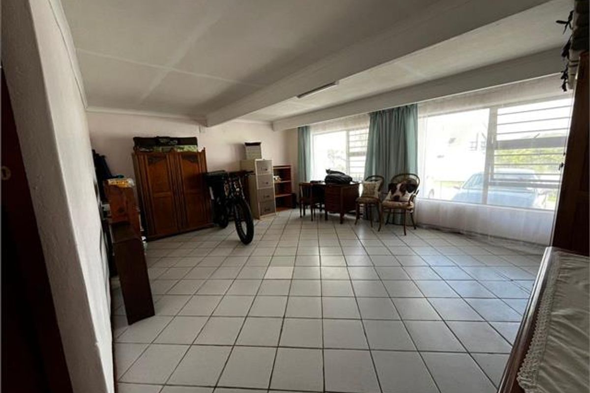 Spacious living area featuring large windows, tiled flooring, and an exposed ceiling beam, offering a bright and versatile space for relaxation.