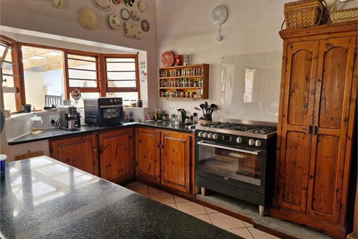 A rustic-style kitchen featuring wooden cabinetry, granite countertops, a gas stove with oven, and a large bay window providing natural light.
