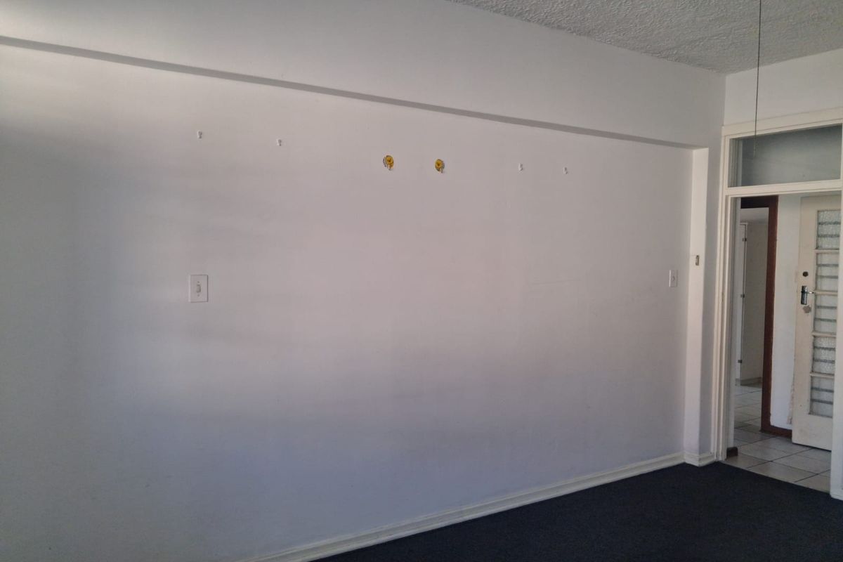 An empty living room featuring a textured ceiling, ceiling fan, and dark carpeting, ready for personalization and staging.