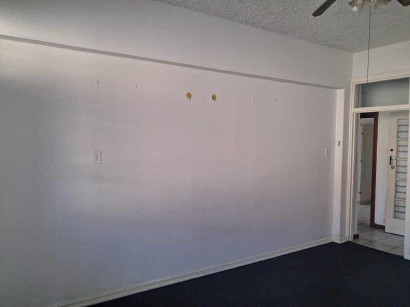 An empty living room featuring a textured ceiling, ceiling fan, and dark carpeting, ready for personalization and staging.