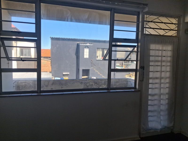 An empty living area featuring large aluminium windows with security bars and a glass door, offering an urban view of neighboring buildings.