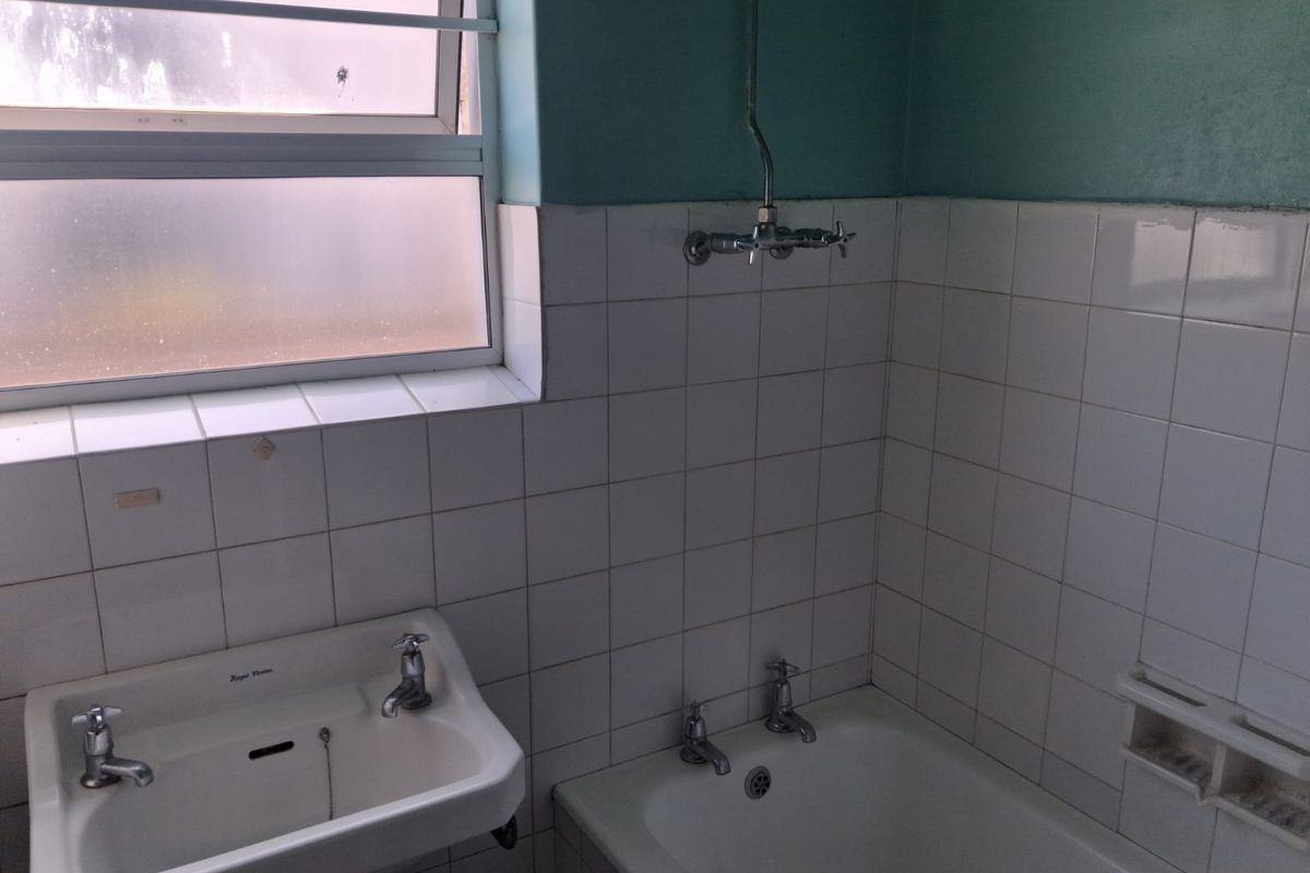 A dated bathroom featuring a wall-mounted basin, bathtub with shower mixer, and tiled splashbacks, offering potential for a modern renovation.