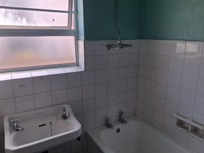 A dated bathroom featuring a wall-mounted basin, bathtub with shower mixer, and tiled splashbacks, offering potential for a modern renovation.