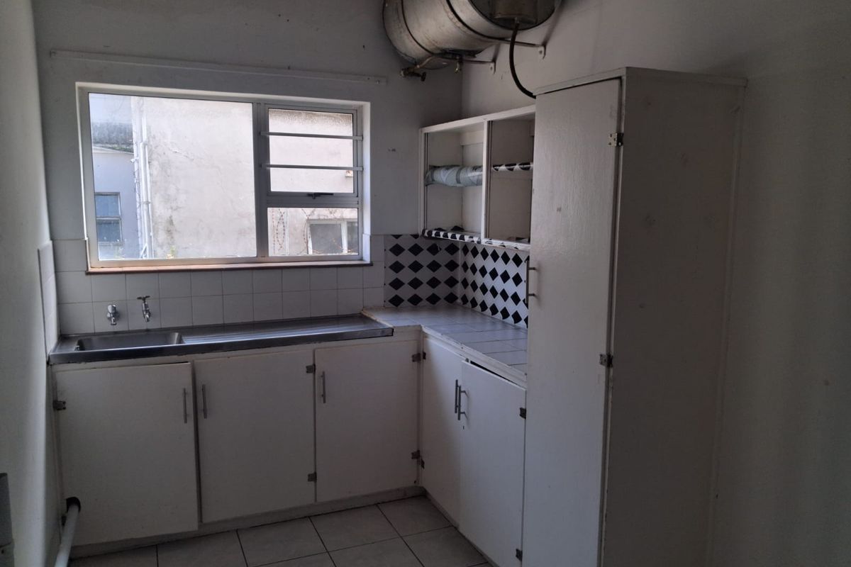 A dated kitchen featuring built-in white cabinetry, a stainless steel sink, tiled backsplash, and an exposed electric water heater.
