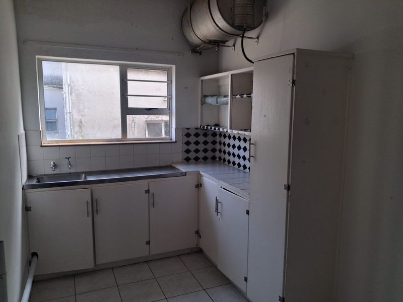 A dated kitchen featuring built-in white cabinetry, a stainless steel sink, tiled backsplash, and an exposed electric water heater.