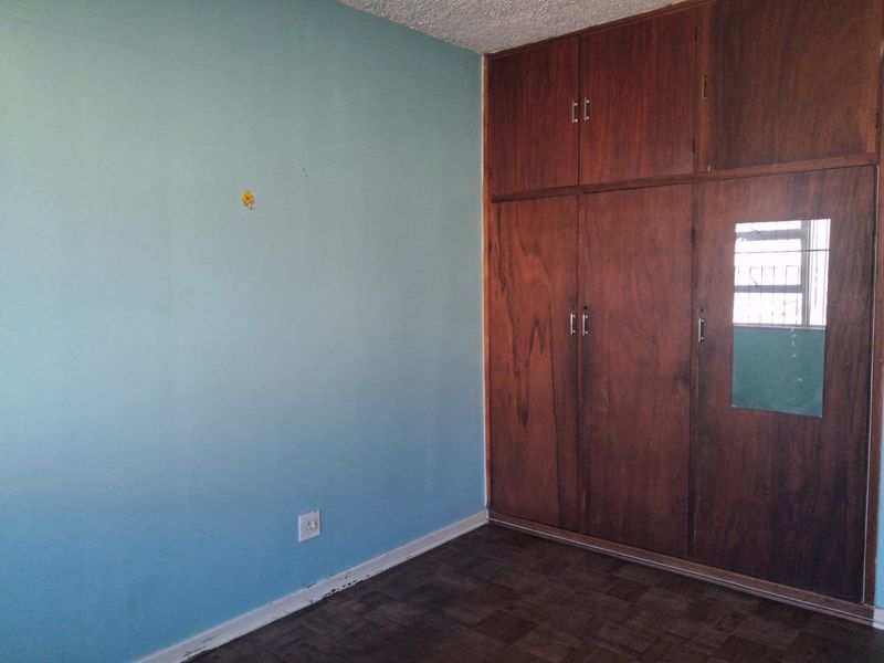 An empty bedroom featuring original parquet flooring, textured ceiling, and floor-to-ceiling built-in wooden cupboards with an integrated mirror.