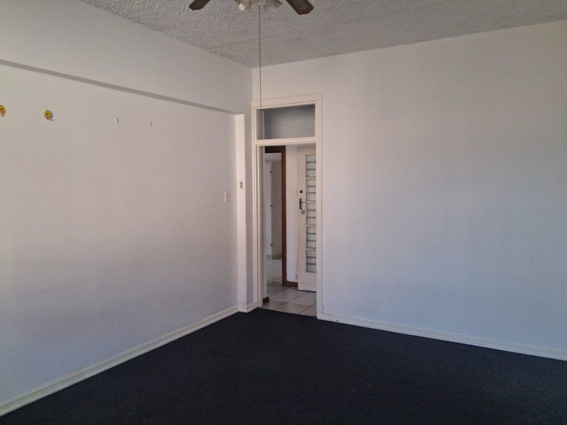 An empty living room featuring dark carpeting, a ceiling fan, and a doorway leading to an adjacent space.