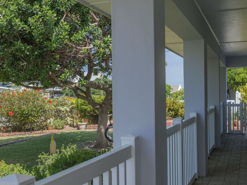 A covered patio area featuring paved flooring, white balustrades, and support pillars, overlooking a well-maintained garden.