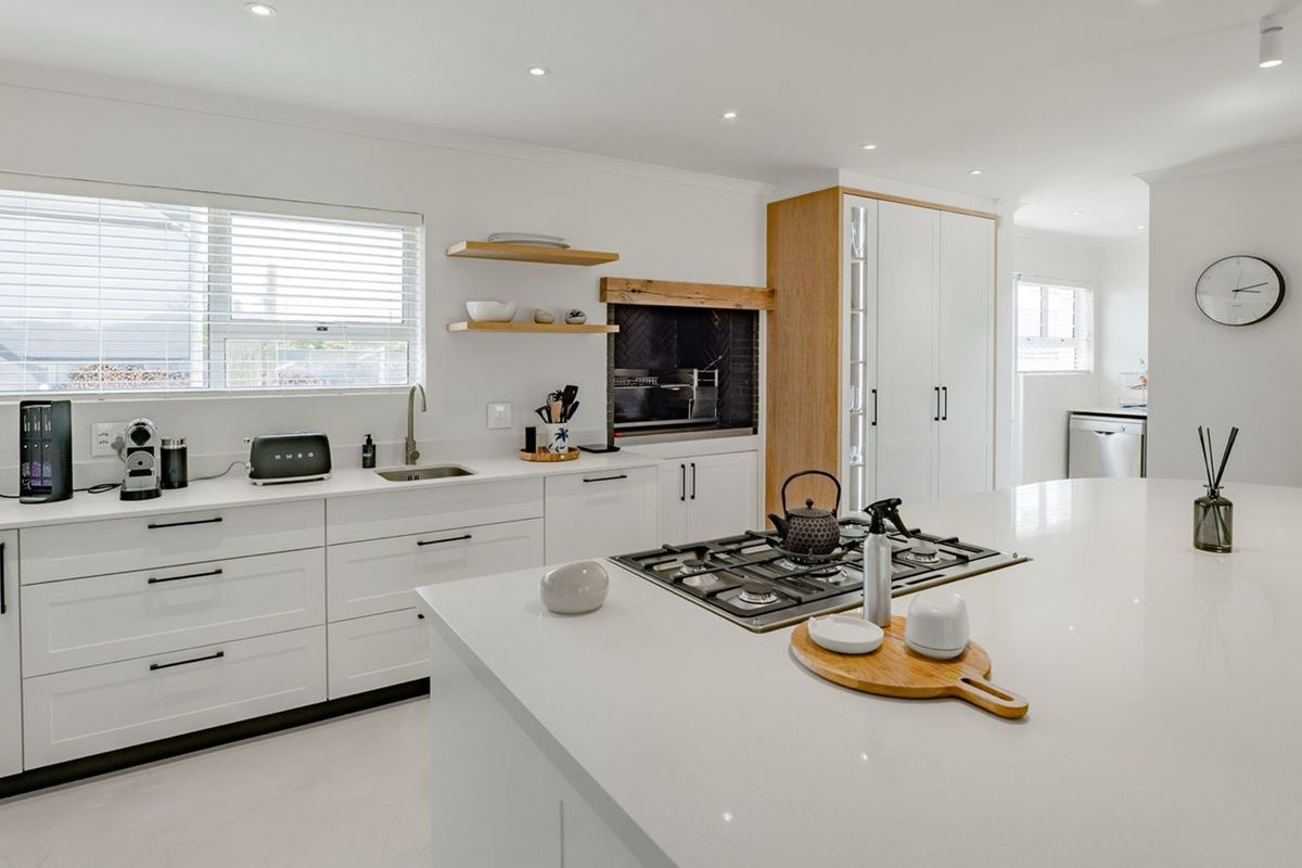 Modern kitchen featuring a large central island, gas cooktop, sleek white cabinetry, and a built-in fireplace, offering a clean and contemporary aesthetic.