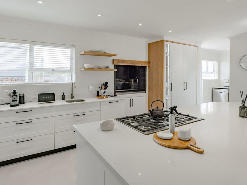 Modern kitchen featuring a large central island, gas cooktop, sleek white cabinetry, and a built-in fireplace, offering a clean and contemporary aesthetic.