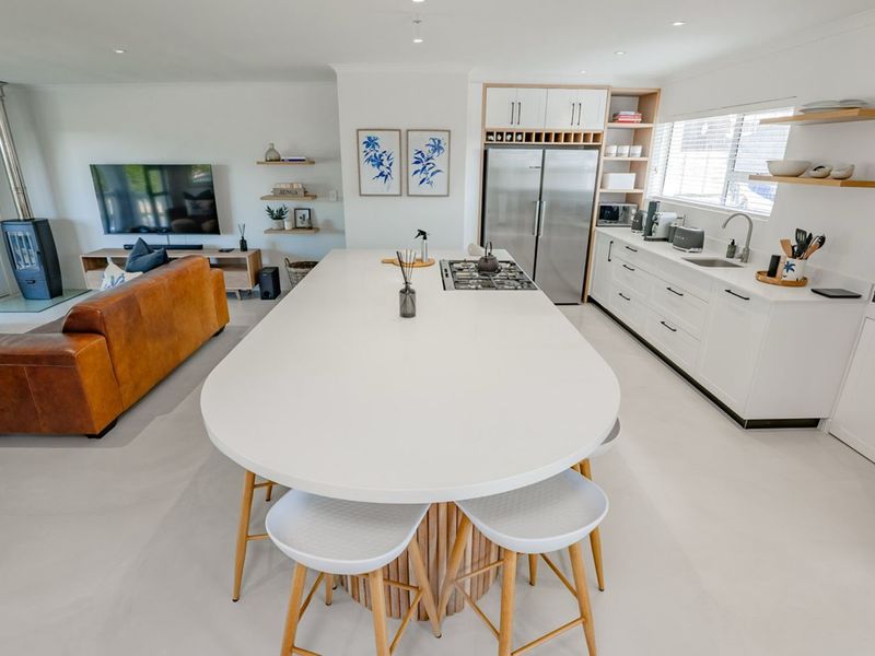 Modern open-plan living area featuring a spacious kitchen island, gas hob, sleek cabinetry, and a cozy wood-burning fireplace in the adjacent lounge space.