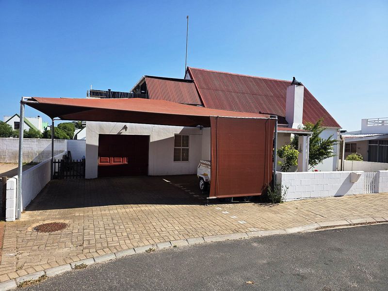 Front exterior view of the house featuring a paved driveway, a shade cloth carport, a garage, and a corrugated metal roof.