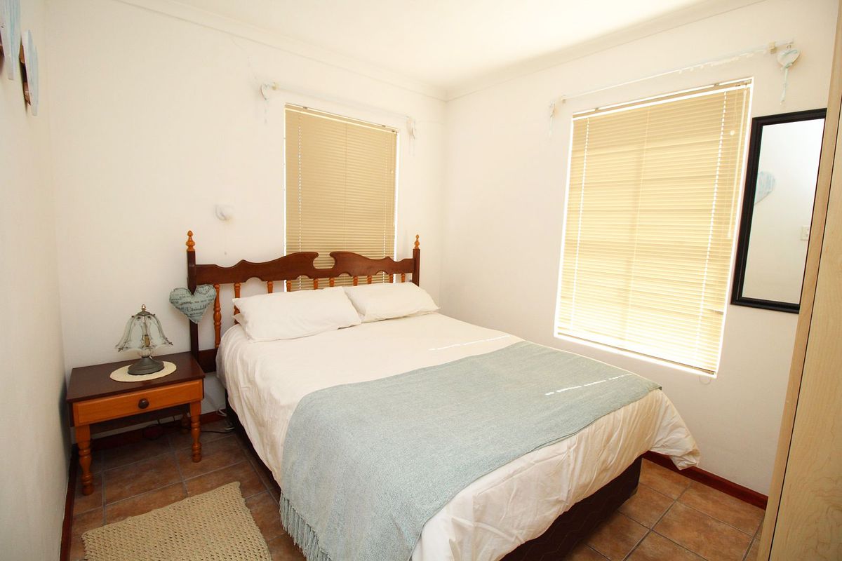 A functional bedroom featuring tiled flooring, dual windows with venetian blinds, and a built-in wardrobe.