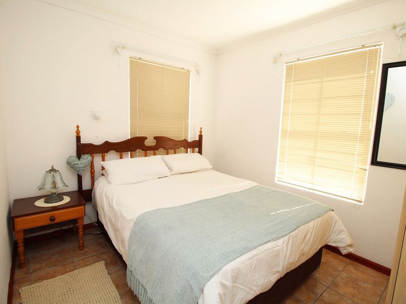 A functional bedroom featuring tiled flooring, dual windows with venetian blinds, and a built-in wardrobe.