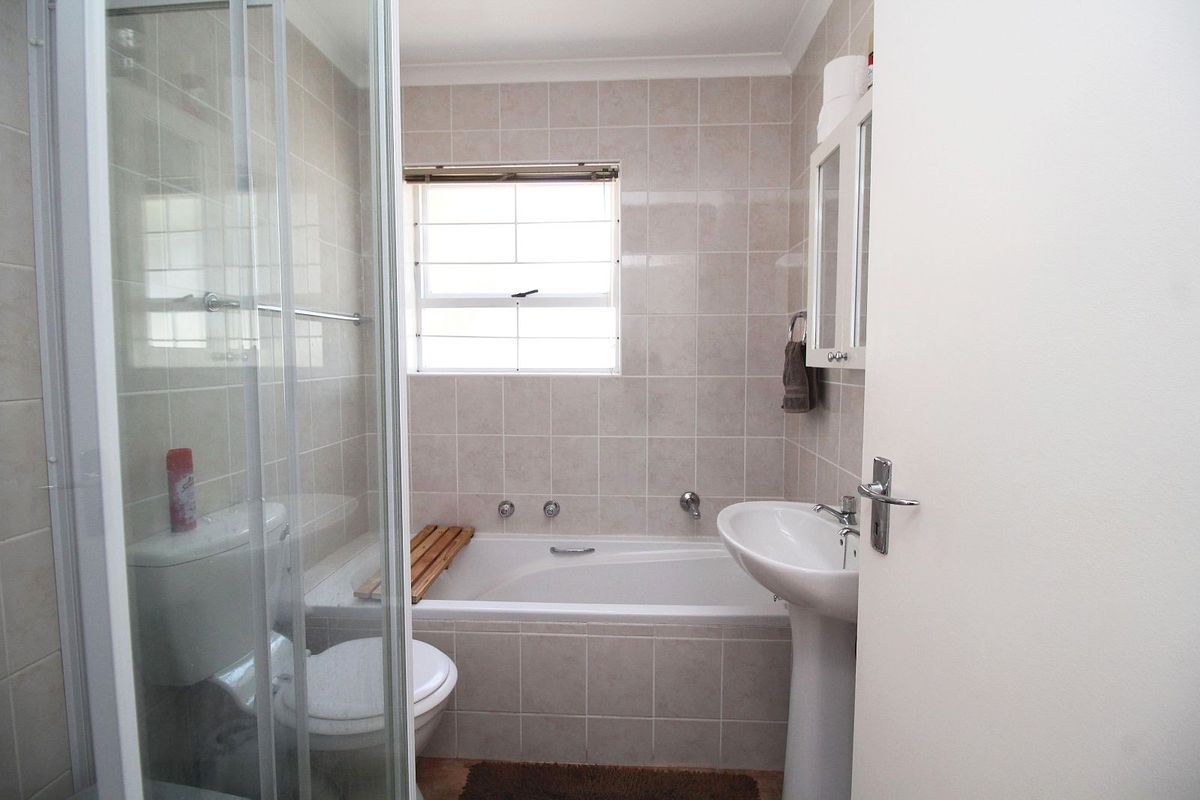 A functional bathroom featuring a pedestal basin, a built-in bathtub, and a separate glass-enclosed shower with neutral wall tiling.