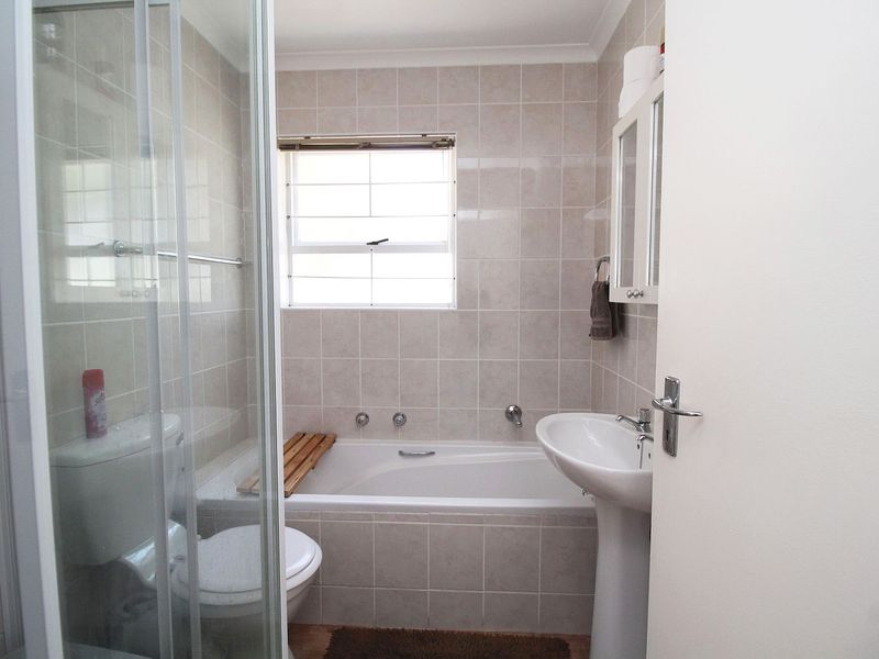 A functional bathroom featuring a pedestal basin, a built-in bathtub, and a separate glass-enclosed shower with neutral wall tiling.
