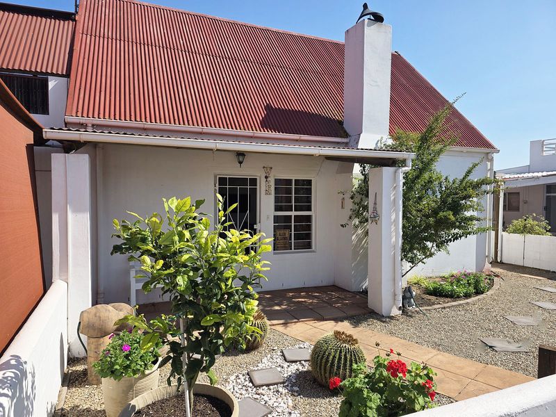 Front facade of a cottage-style home featuring a red corrugated metal roof, a covered patio entrance, and a masonry chimney.