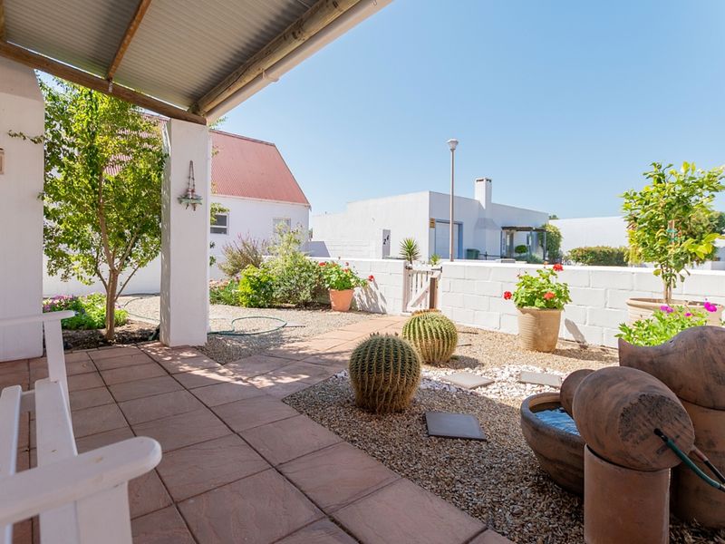 A covered patio area featuring tiled flooring and a corrugated roof, overlooking a low-maintenance gravel garden with a masonry boundary wall.