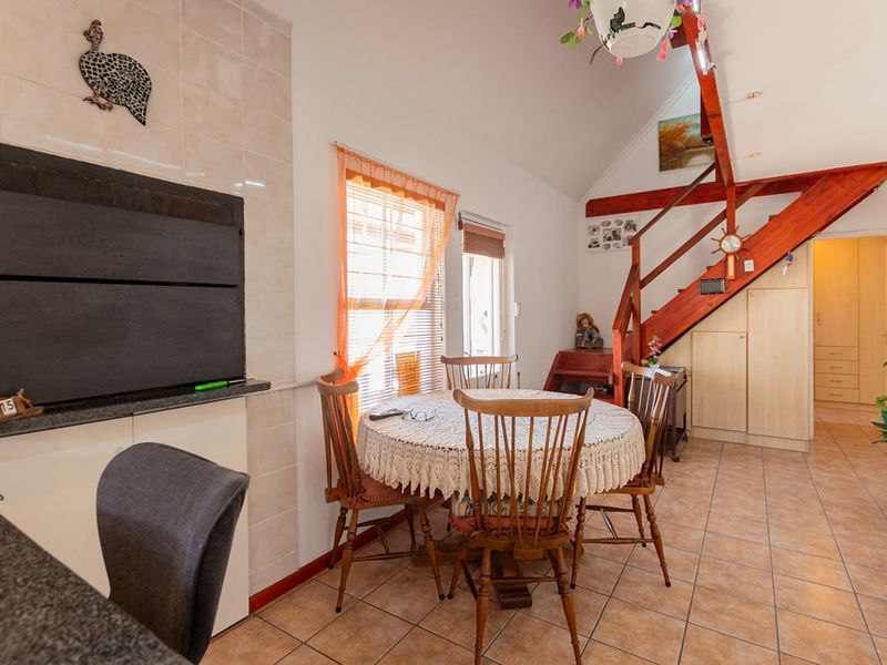 Open-plan living area featuring a built-in braai, tiled flooring, and a wooden staircase leading to an upper level.