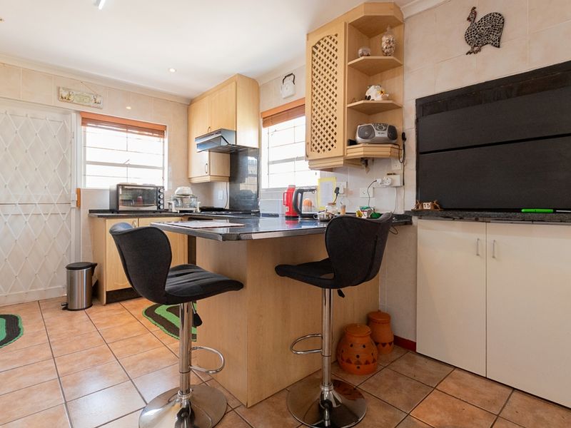 A functional kitchen featuring light wood cabinetry, granite countertops, tiled flooring, and a built-in braai area with direct access to the exterior.