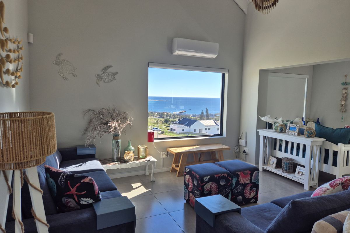 Bright living room featuring vaulted ceilings, tiled flooring, a wall-mounted air conditioner, and a large picture window with expansive coastal views.