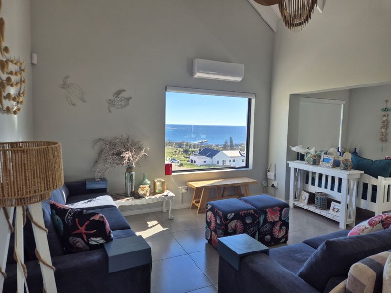 Bright living room featuring vaulted ceilings, tiled flooring, a wall-mounted air conditioner, and a large picture window with expansive coastal views.