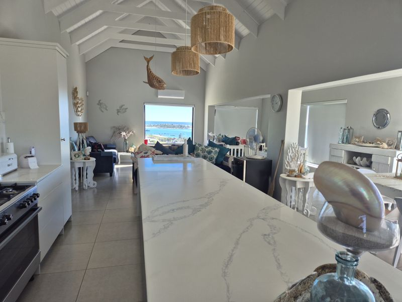 Spacious open-plan living area featuring a vaulted ceiling with exposed rafters, a large stone kitchen island, and stunning coastal views.