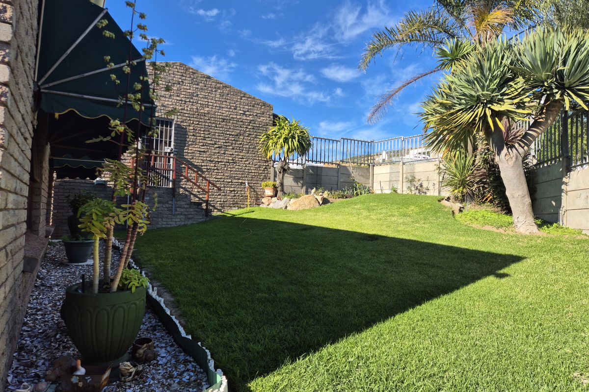 A well-maintained rear garden featuring a manicured lawn, brick exterior walls, protective awnings, and established landscaping with secure perimeter fencing.