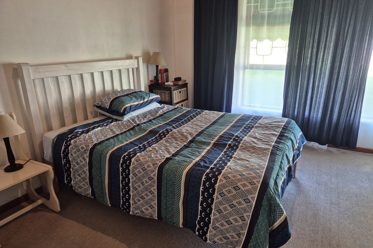 A functional bedroom featuring carpeted flooring and a window fitted with security bars, providing natural light and a secure environment.