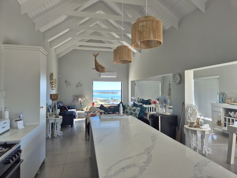 Spacious open-plan living area featuring a vaulted ceiling with exposed rafters, a modern kitchen island with stone countertops, and scenic coastal views.