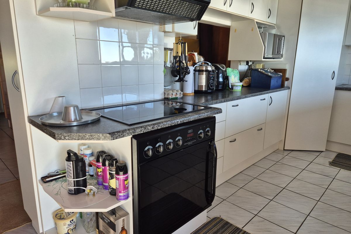 A functional kitchen featuring built-in cabinetry, an electric cooktop with extractor fan, tiled backsplash, and ceramic floor tiles.