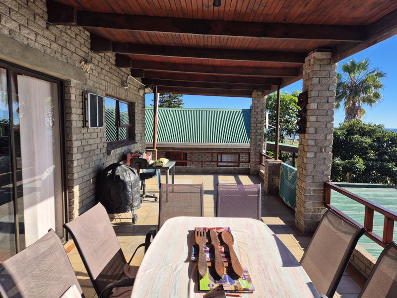 Covered outdoor patio featuring exposed timber beams, facebrick columns, and tiled flooring, providing a functional space for outdoor dining and relaxation.
