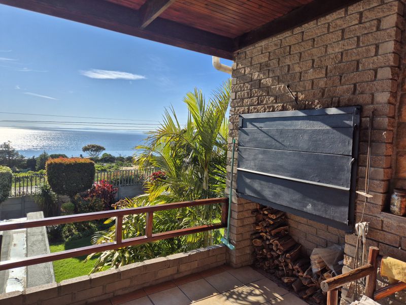Covered patio featuring a built-in braai, timber ceiling, and tiled flooring, offering scenic ocean views and direct access to the garden.