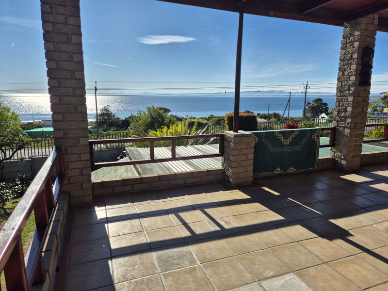 A spacious covered patio featuring tiled flooring, brick pillars, and timber railings, offering expansive ocean views.