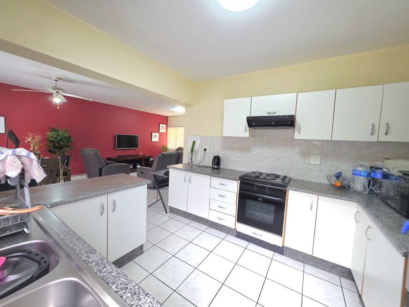 Open-plan kitchen and living area featuring white cabinetry, granite countertops, electric stove, and tiled flooring, creating a functional and connected living space.
