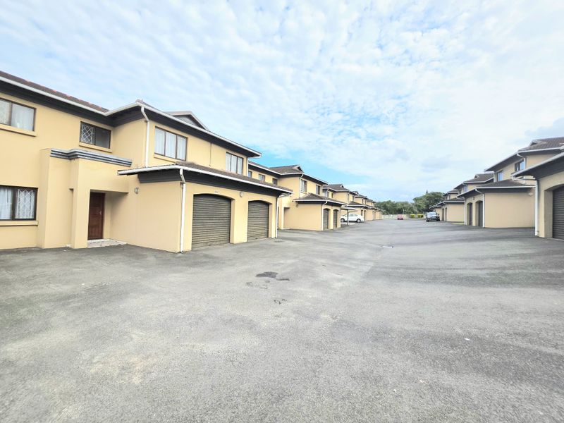 A view of the townhouse complex driveway featuring multiple units with individual roller garage doors and paved access.