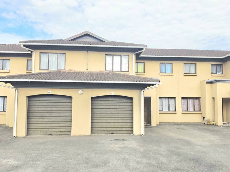 Front elevation of a townhouse complex featuring two roller garage doors, tiled roofing, and an asphalt driveway area.